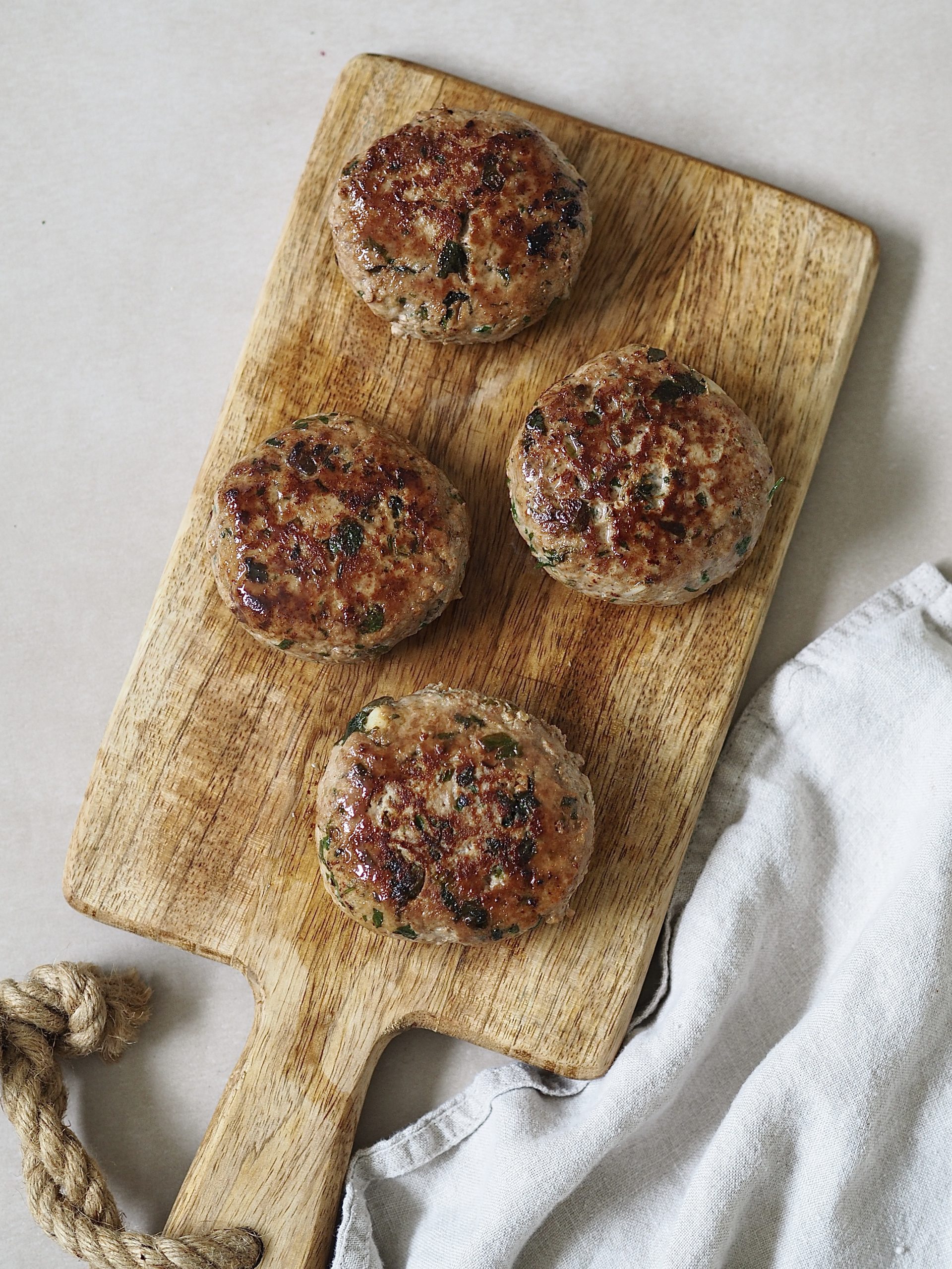 Four cooked chicken burgers on a wooden serving board. 