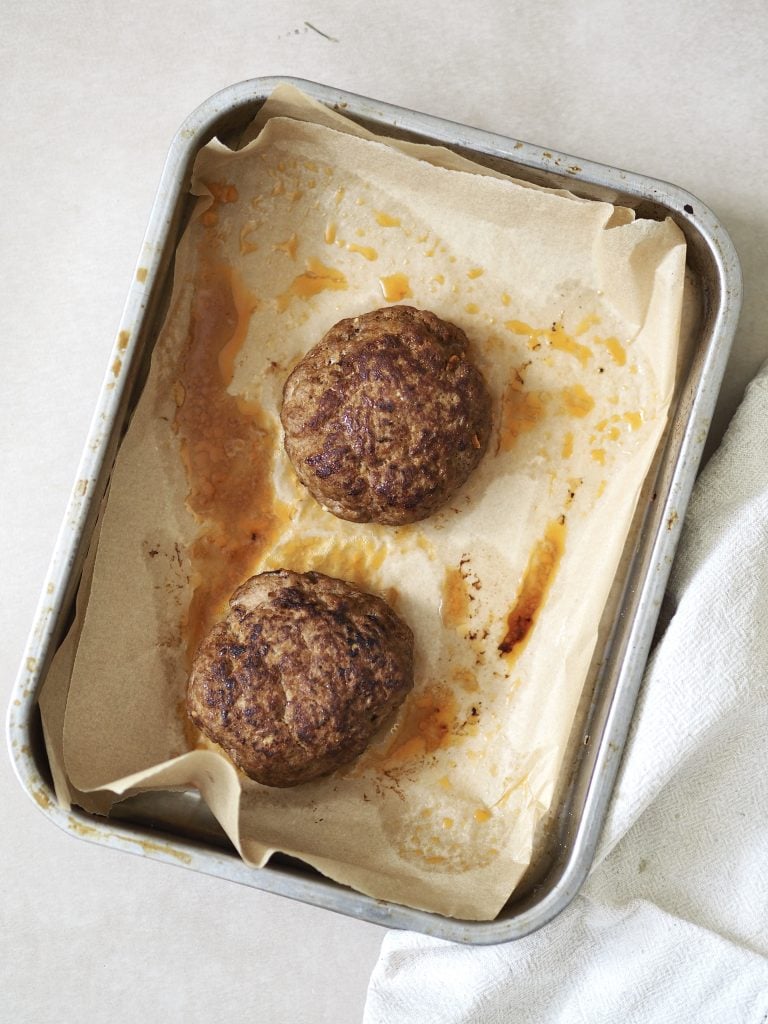 Two cooked lamb burgers on a lined oven tray.