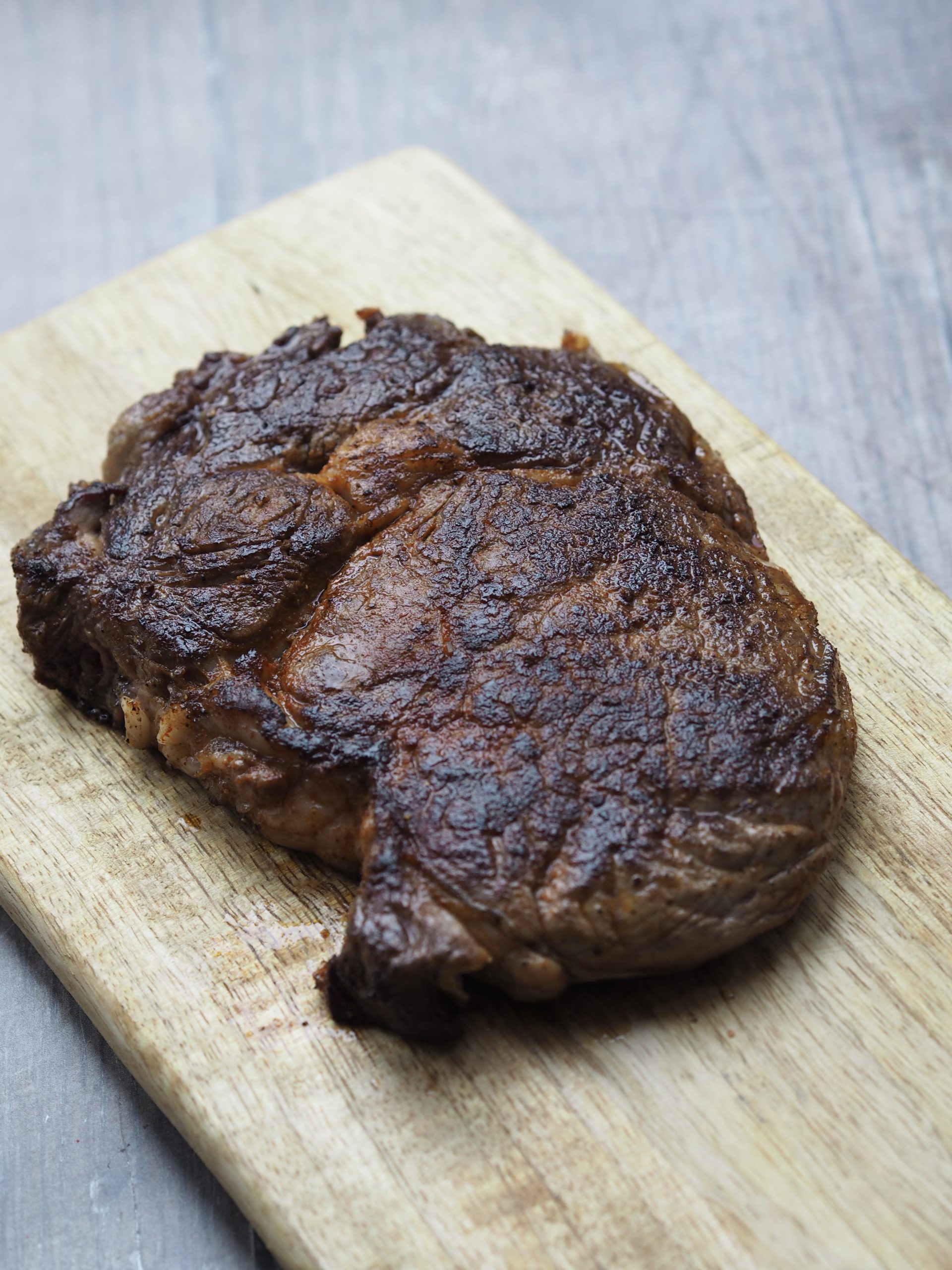 Cooked rib eye steak resting on a wooden cutting board.