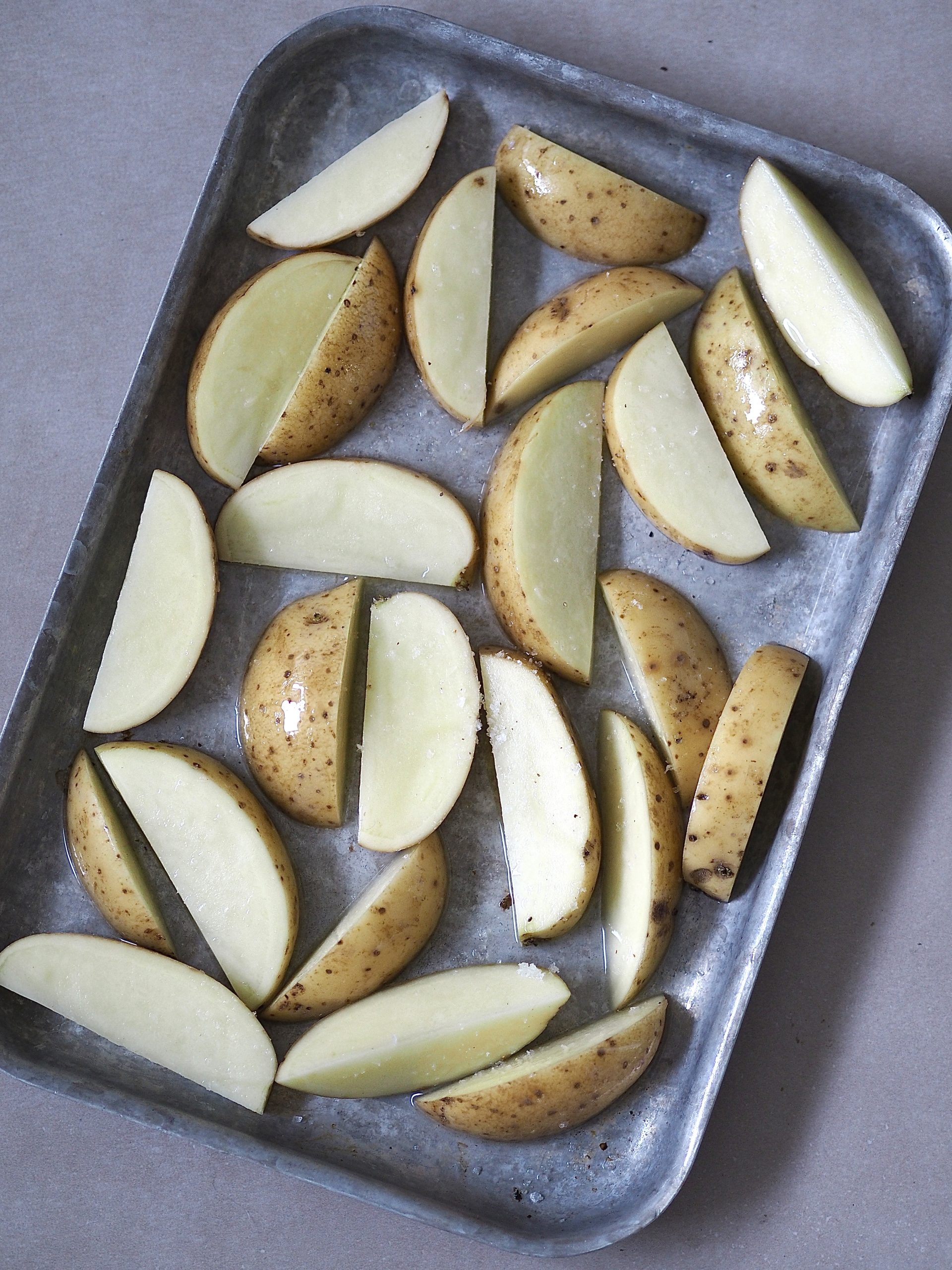 Raw potato wedges on a dark metal baking tray.