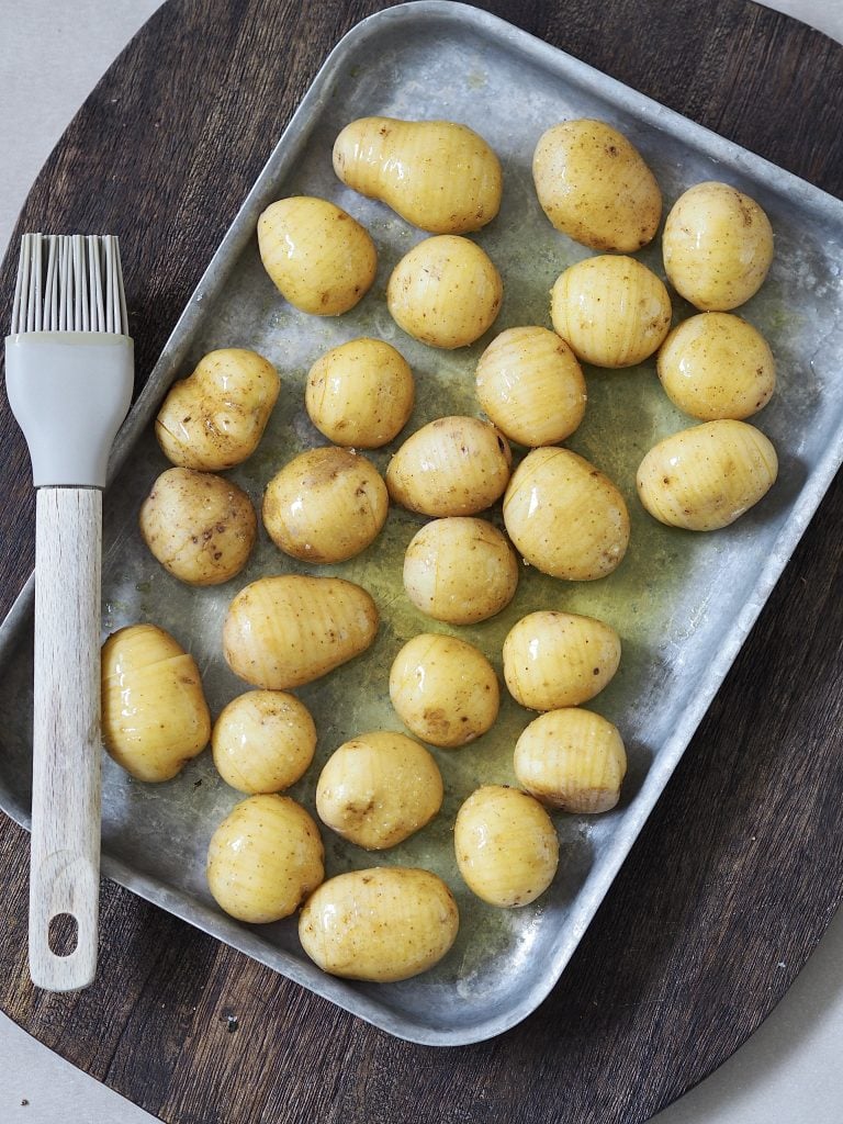 Uncooked hasselback potatoes on a baking tray.