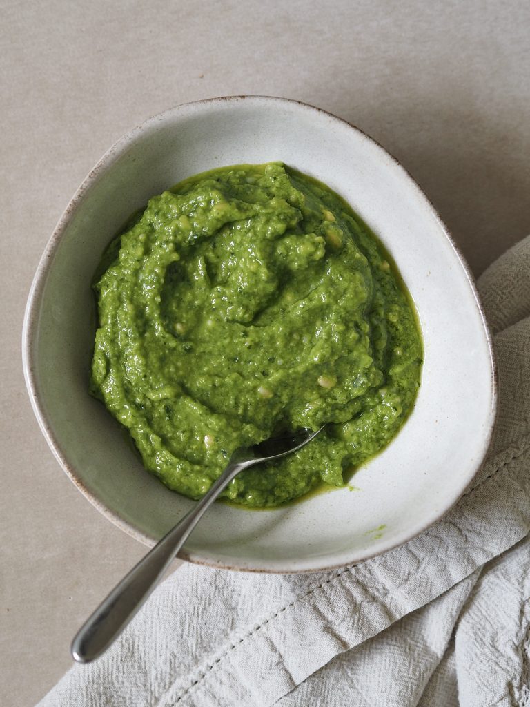 White bowl of green pesto with a silver spoon.