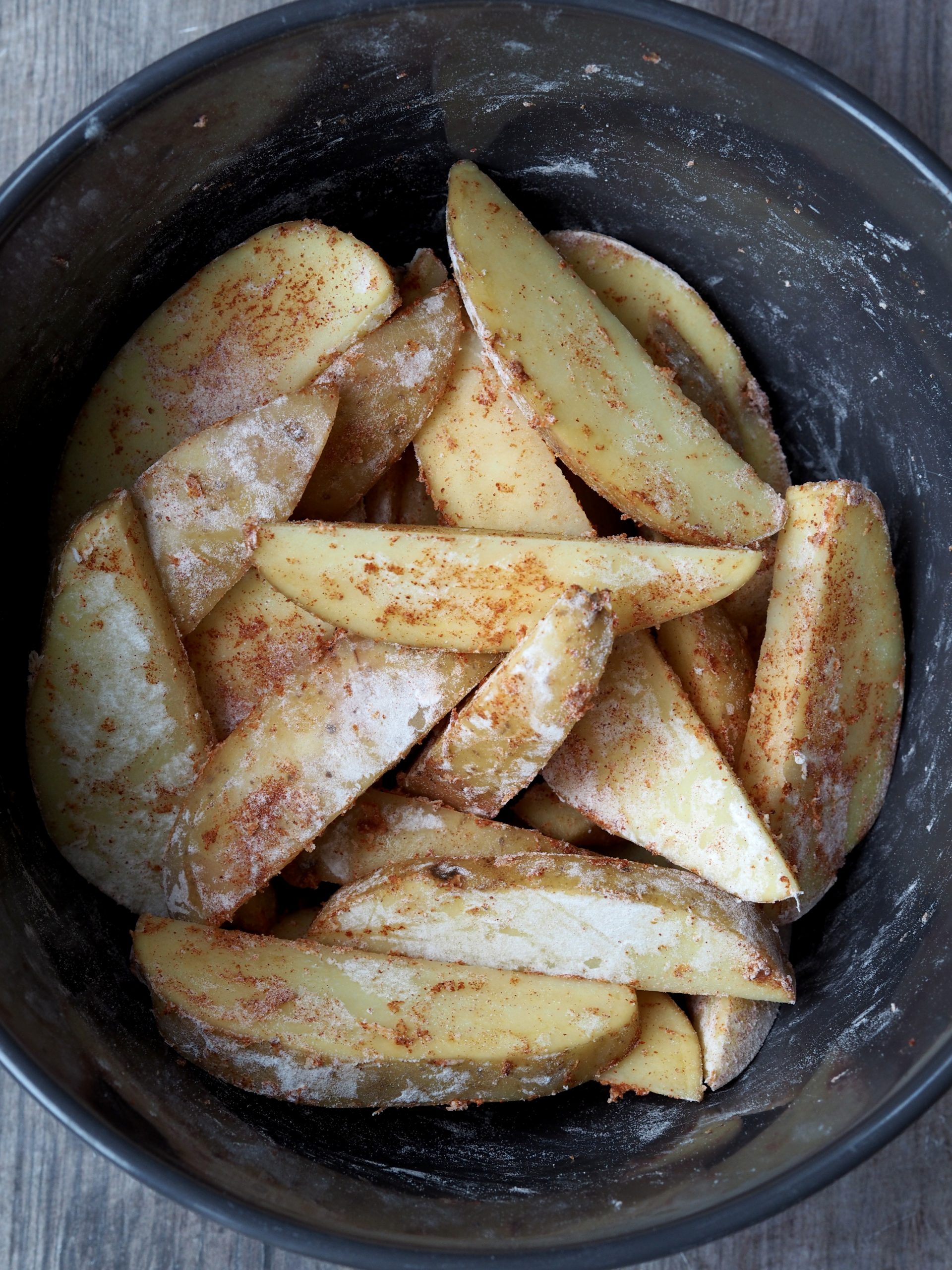 Bowl of uncooked potato wedges tossed with flour and paprika.