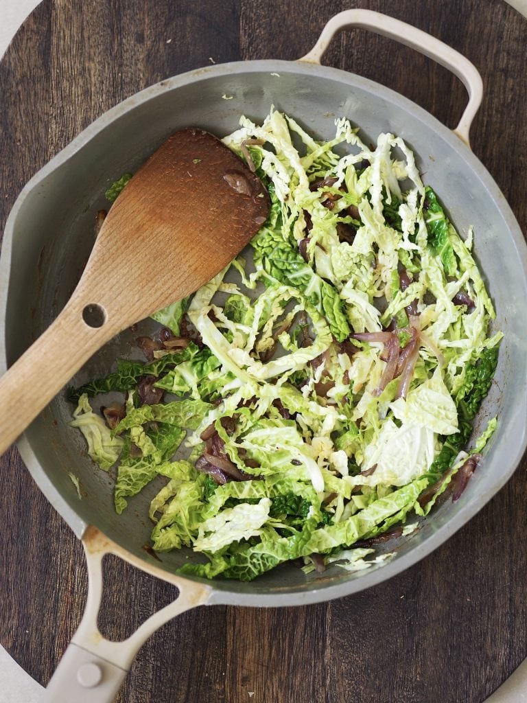 Shredded greens being stirred in a frying pan.