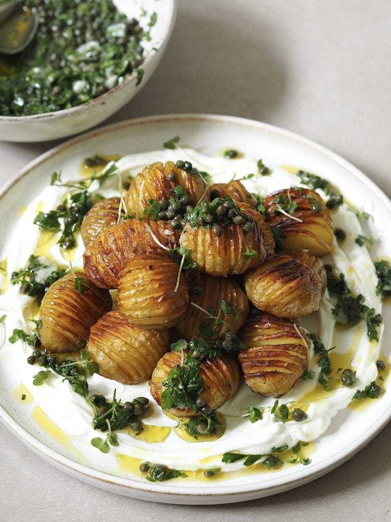 Hasselback potatoes with salsa verde on a plate of labneh.