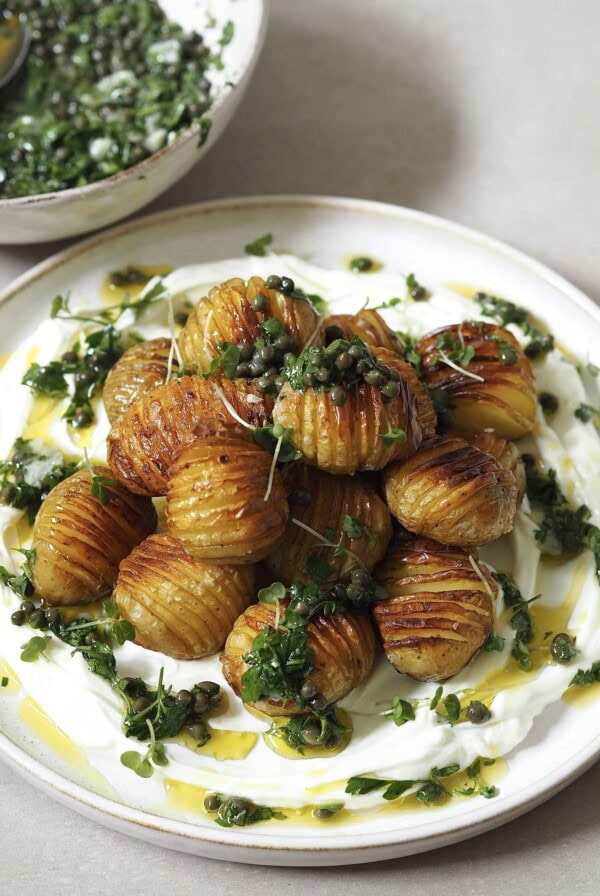 Hasselback potatoes with salsa verde on a plate of labneh.