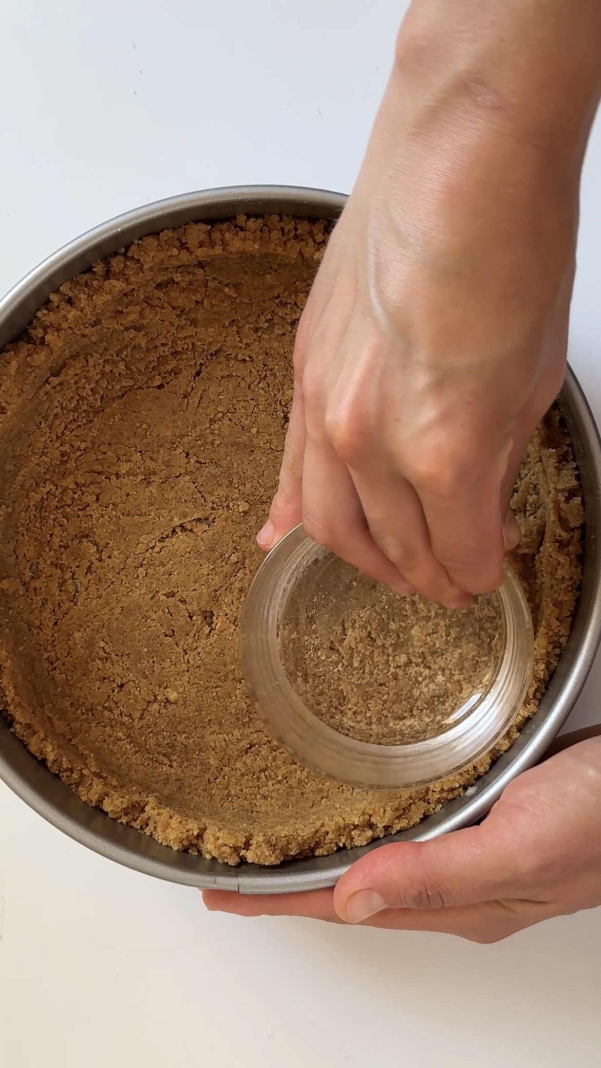 woman pushing a glass around the edge of creme brulee cheesecake crust