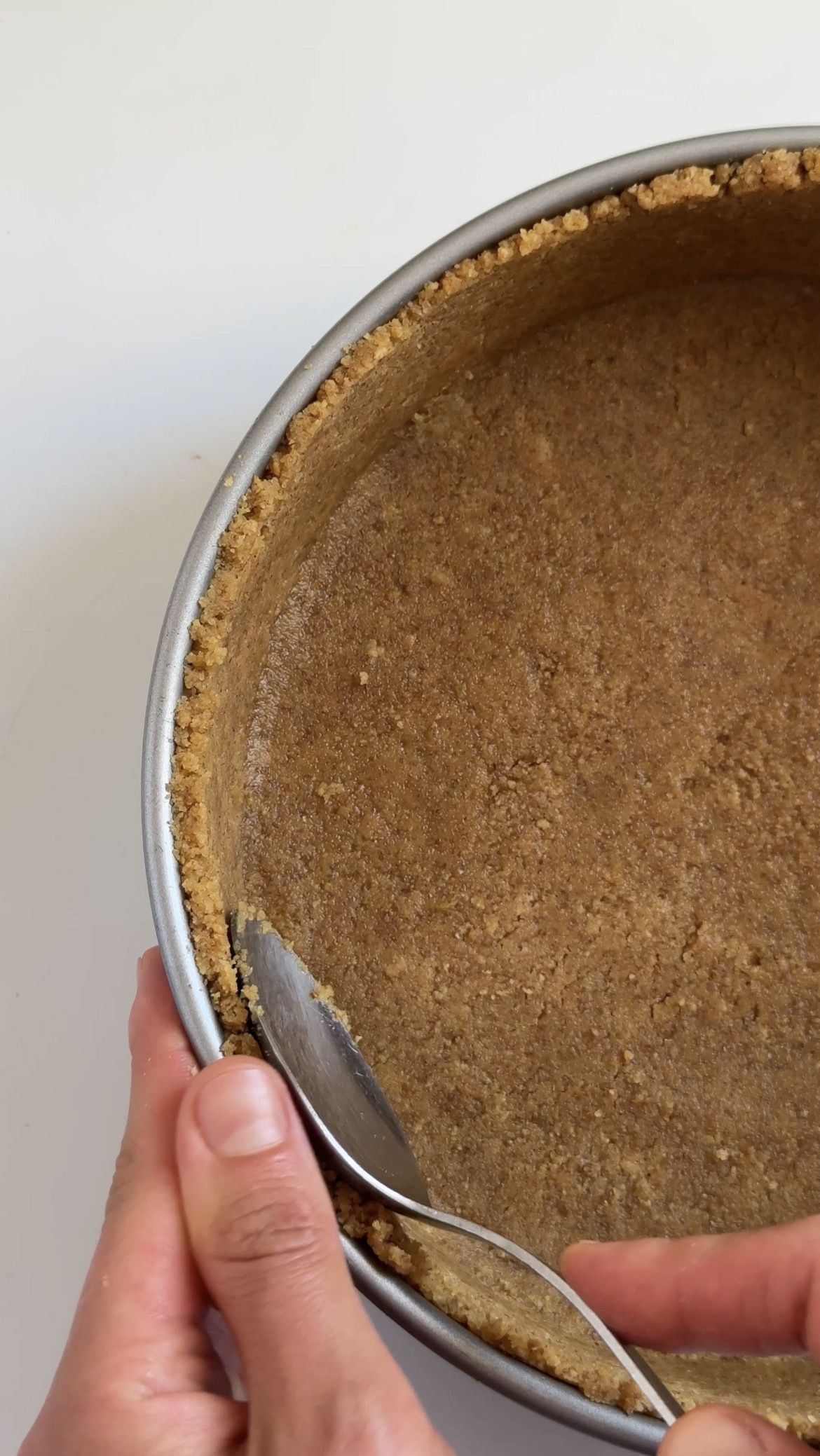 woman pushing a spoon around the edge of creme brulee cheesecake crust