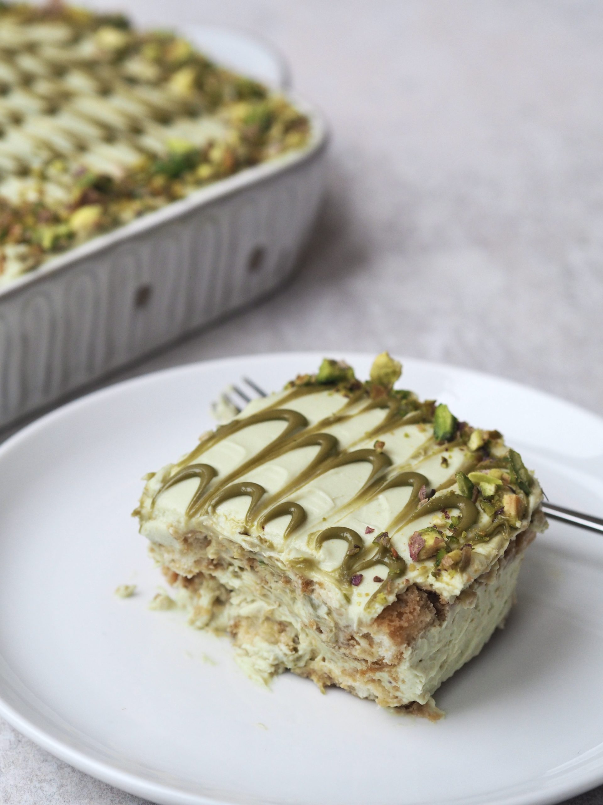 pistachio tiramisu in white dish with slice removed