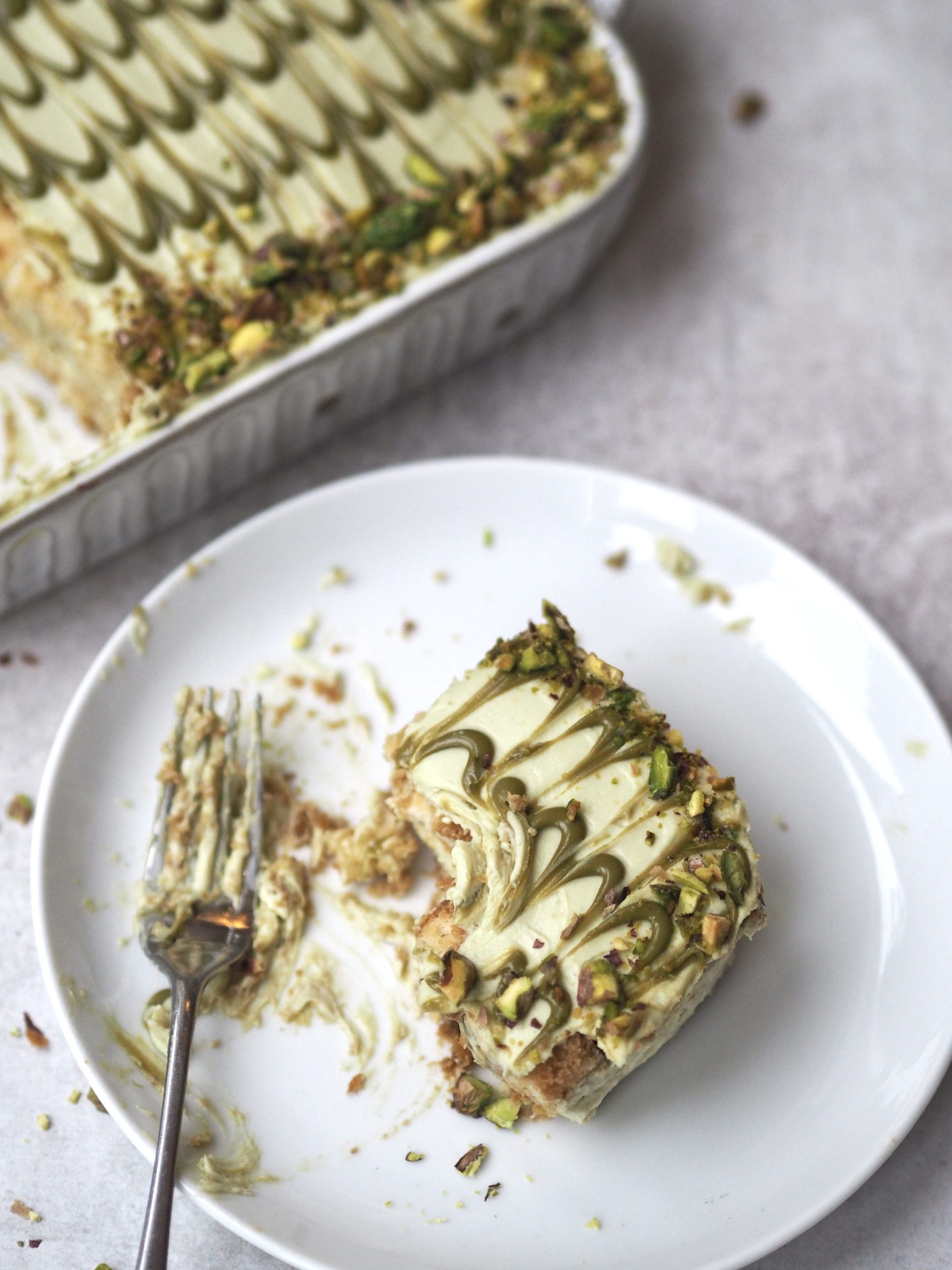 pistachio tiramisu in white dish with slice removed