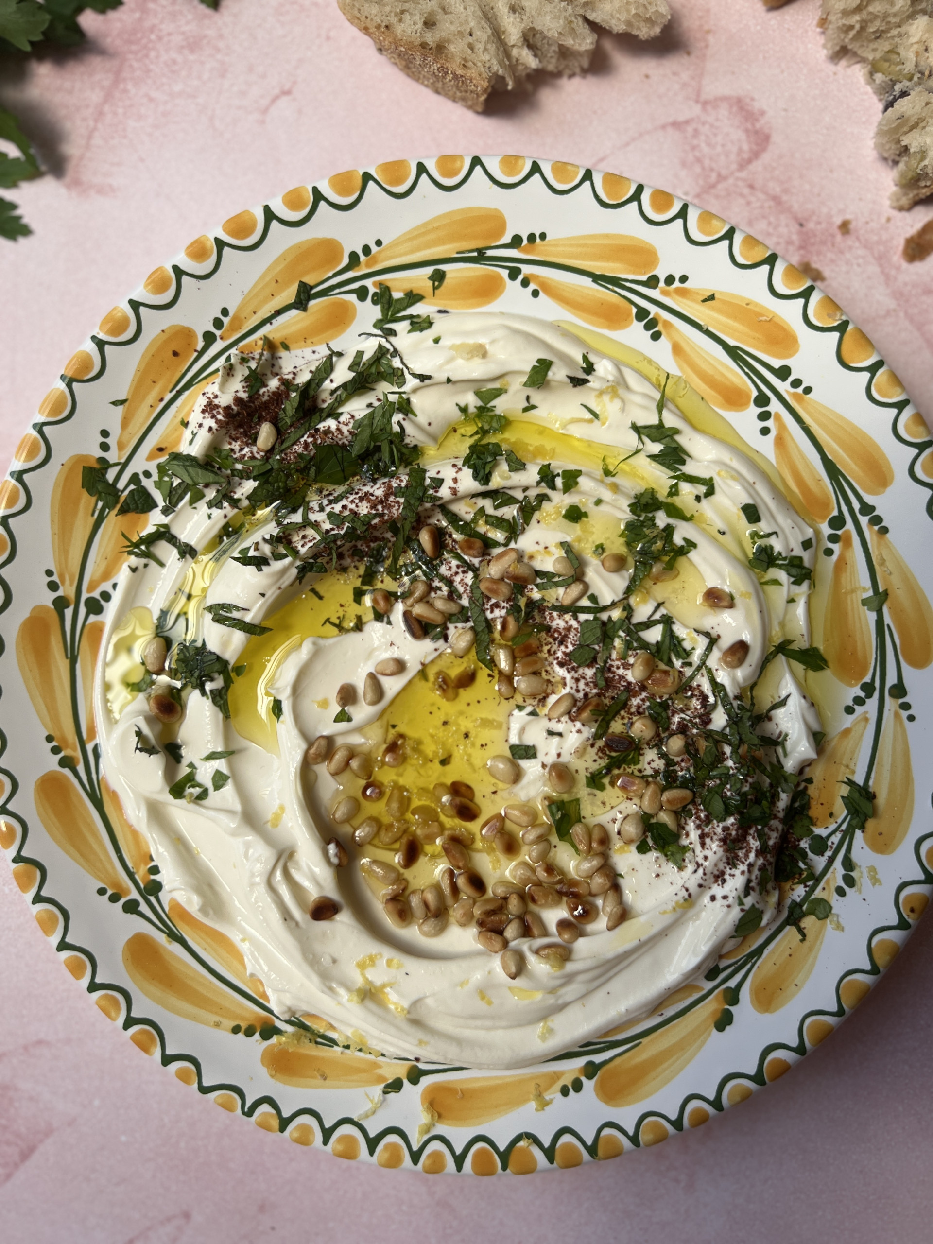 garlic labneh with pine nuts and parsley on a yellow and green plate