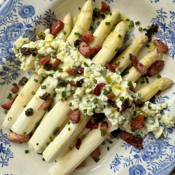 white asparagus topped with bacon on blue and white plate