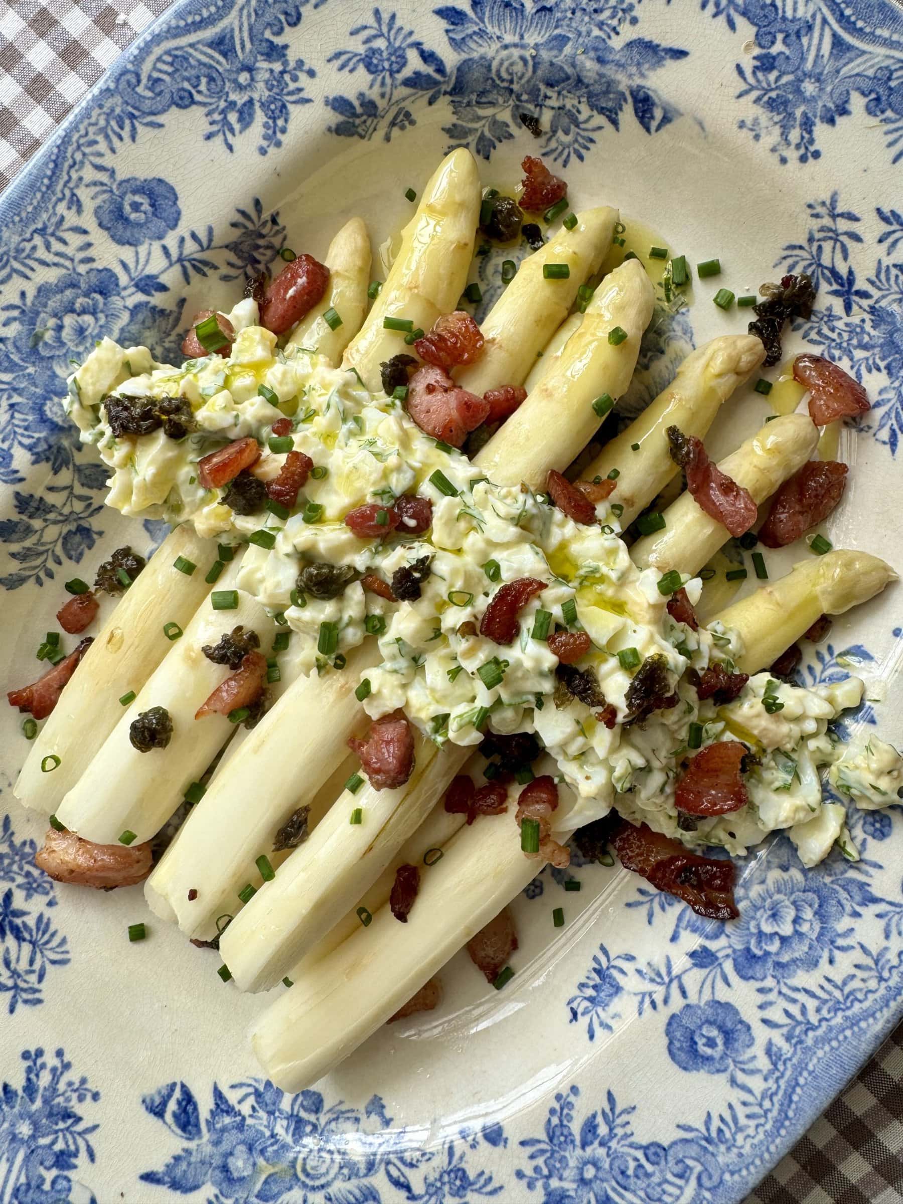 white asparagus topped with bacon on blue and white plate