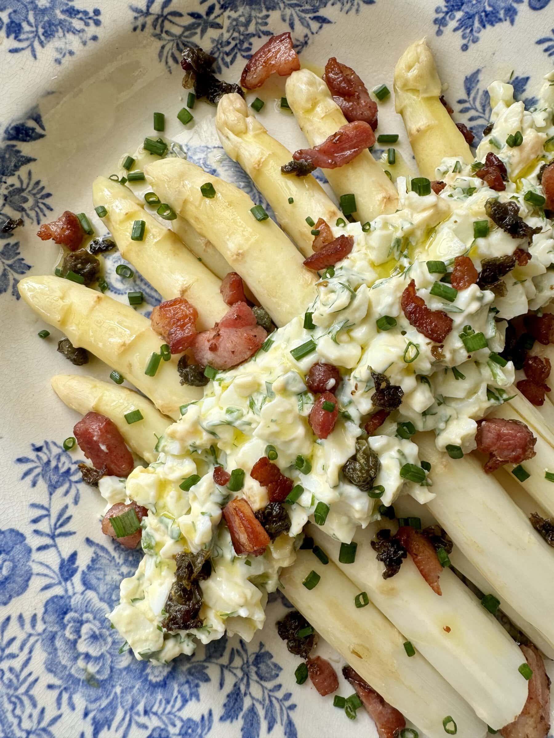 white asparagus topped with bacon on blue and white plate