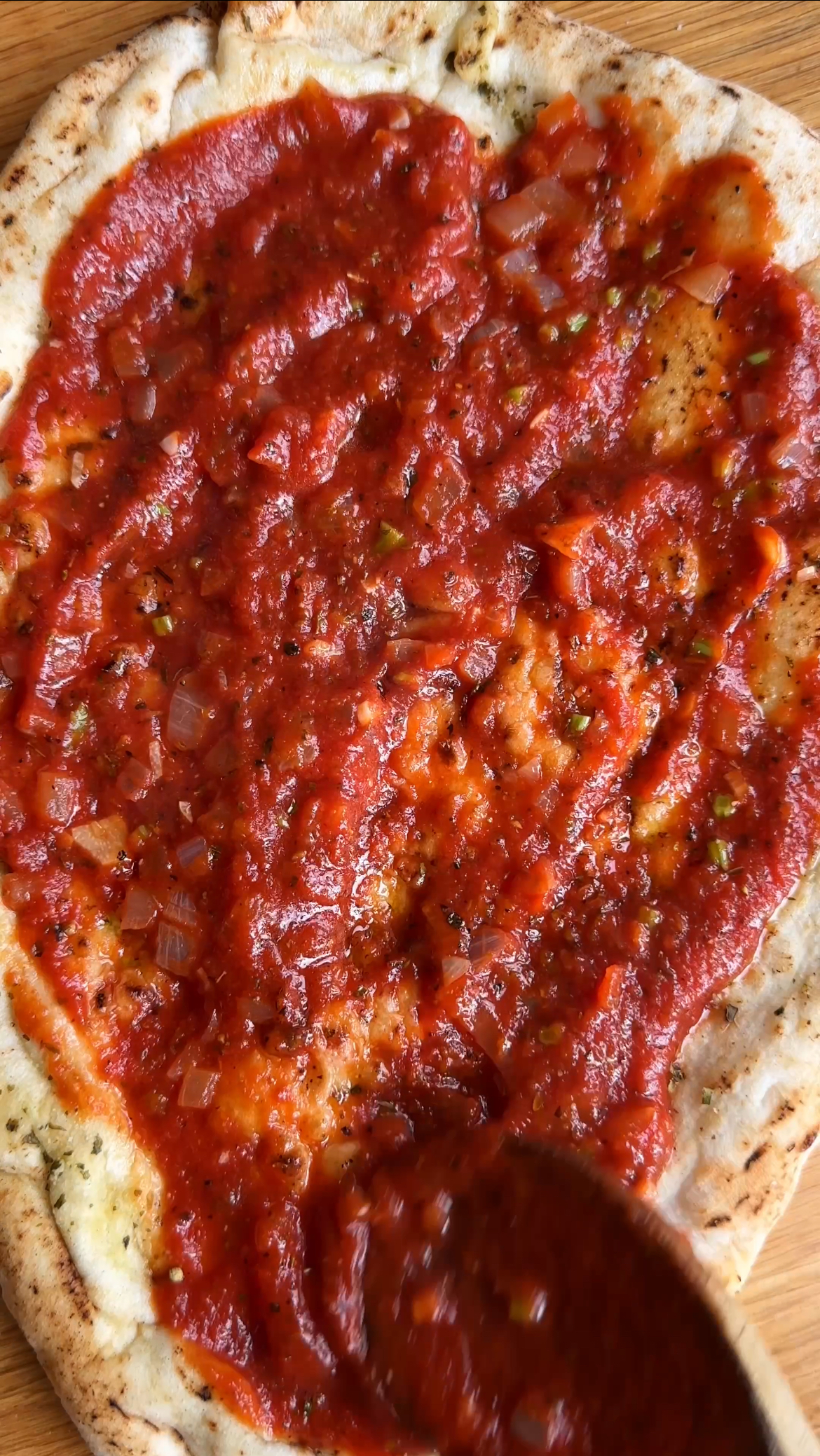 adding tomato sauce to a flatbread