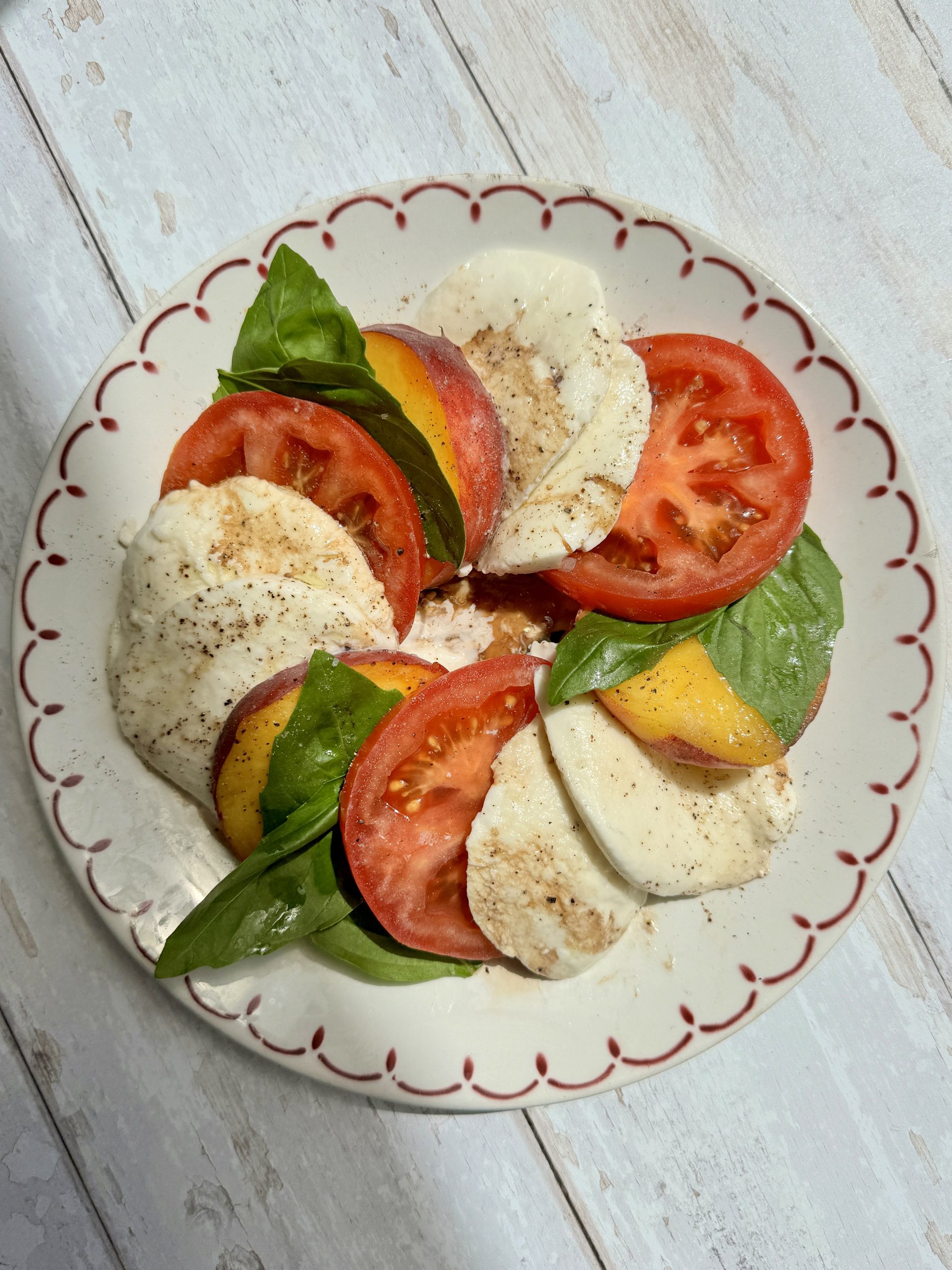 peach caprese on a white plate with red rim