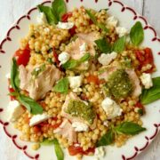 salmon with pesto crust and roasted tomato giant couscous salad on a plate.
