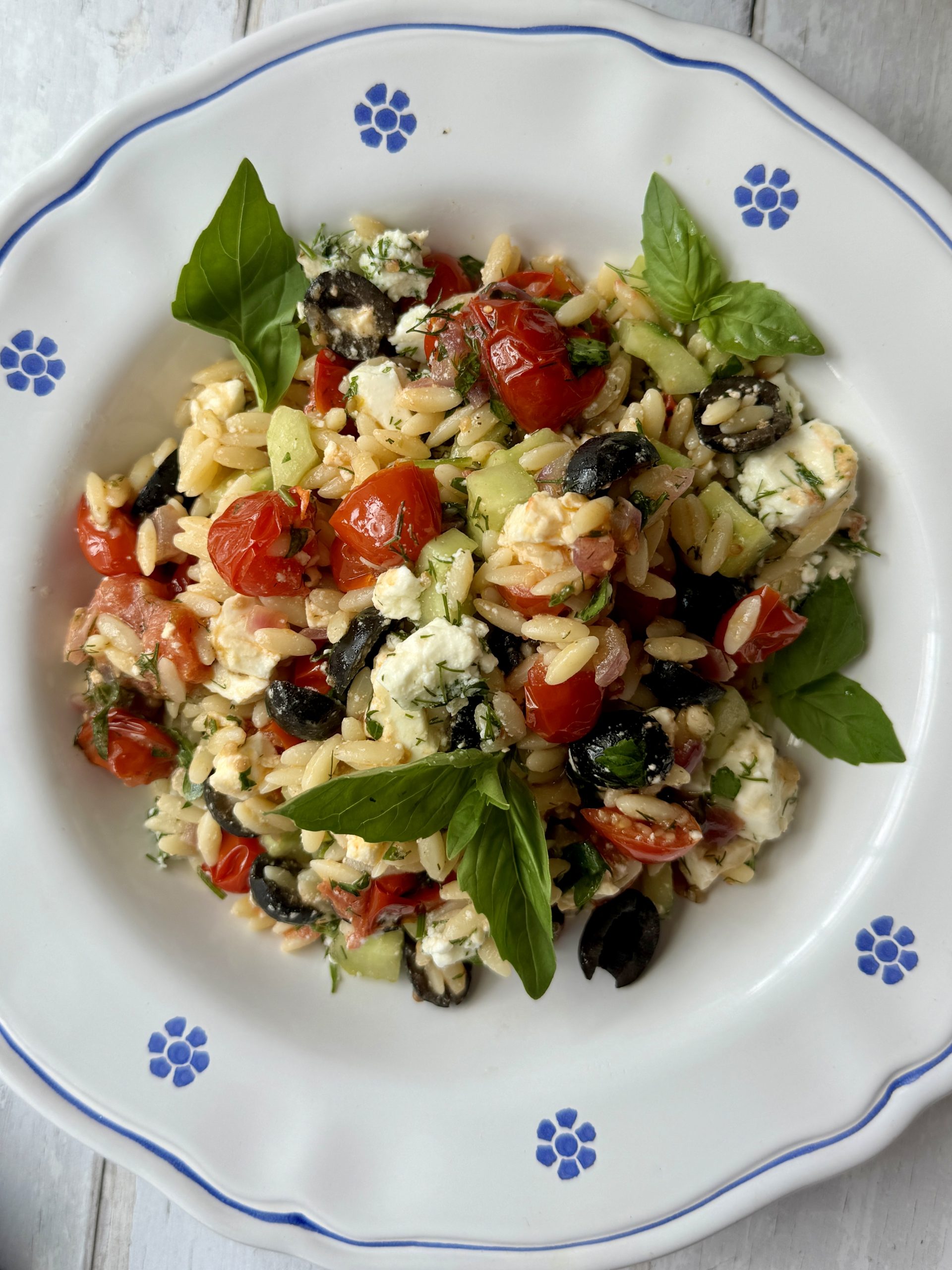 greek pasta salad in white bowl with blue flowers