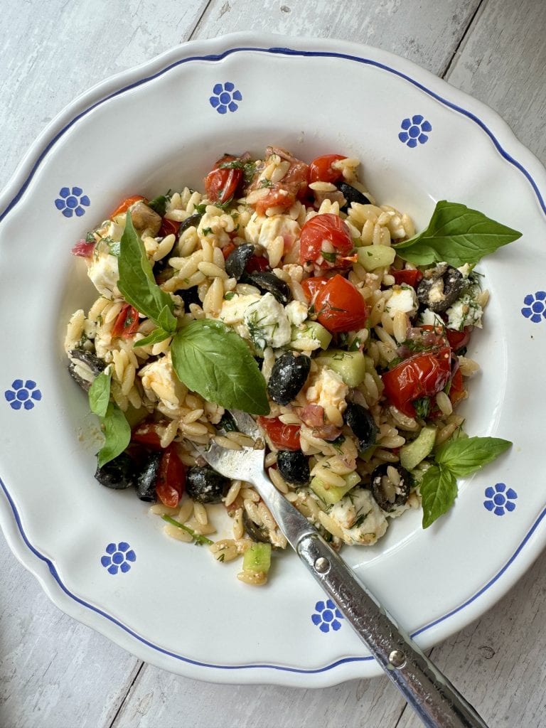 greek pasta salad in white bowl with blue flowers with a fork in the plate