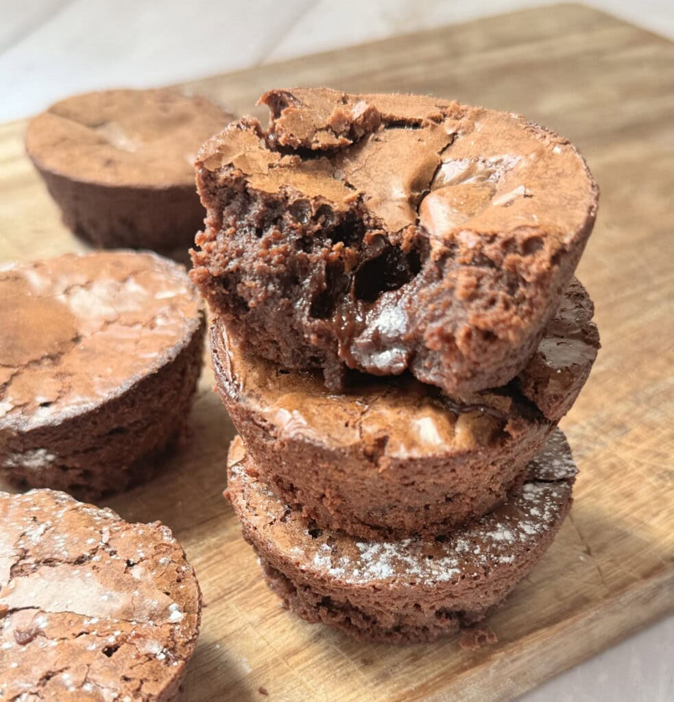 a stack of brownie bites on a wooden chopping board.