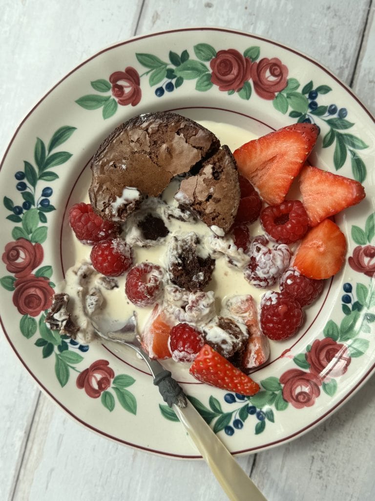 a brownie bite in a floral bowl with cream and berries