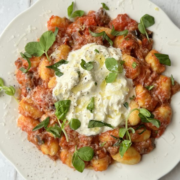 gnocchi alla norma on a white plate with burrata and fresh basil on top