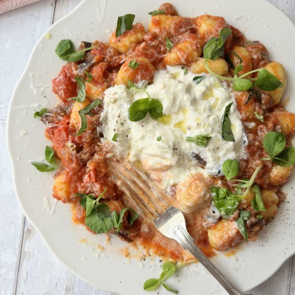 gnocchi alla norma on a white plate with burrata and fresh basil on top