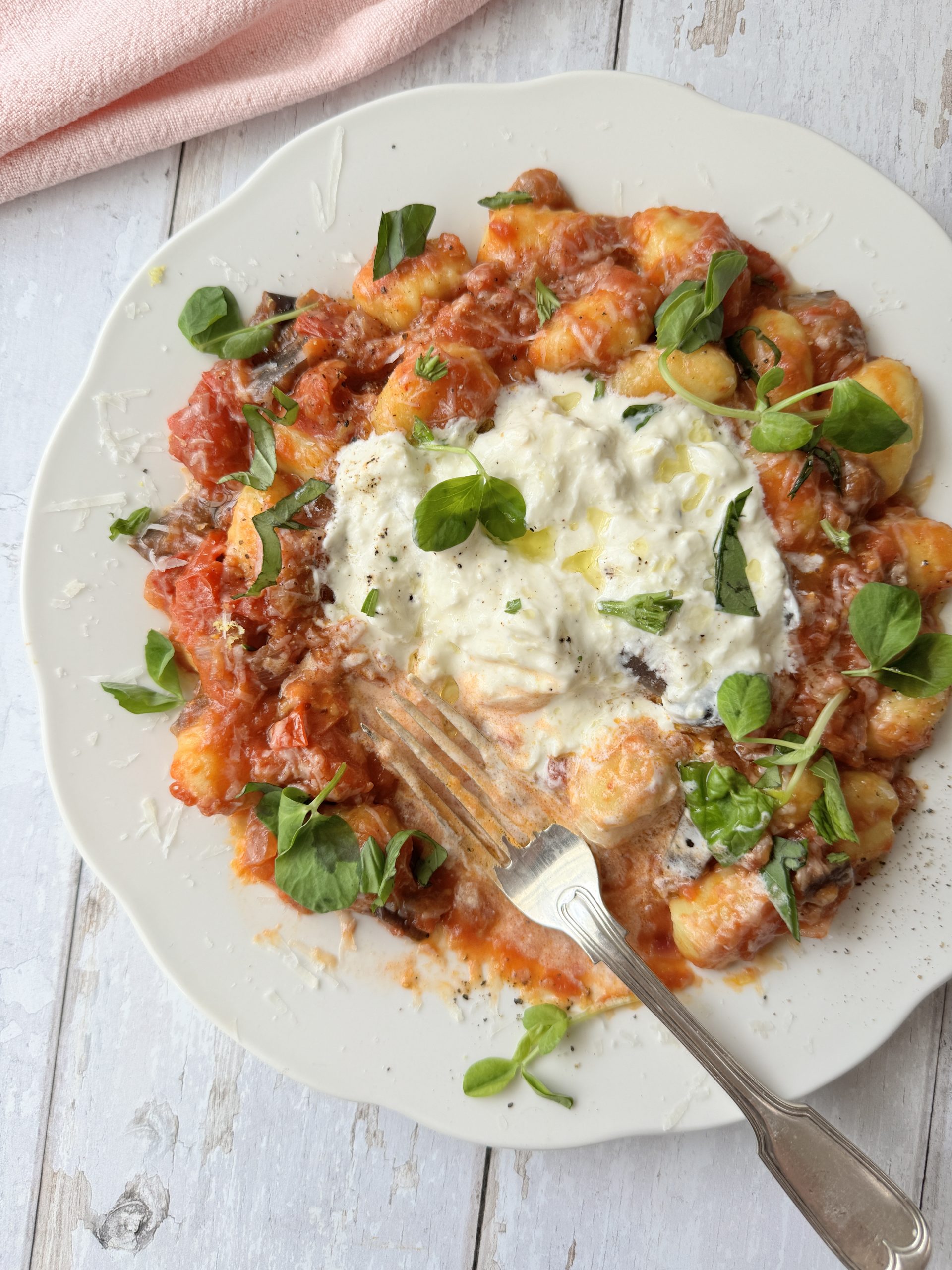 gnocchi alla norma on a white plate with burrata and fresh basil on top