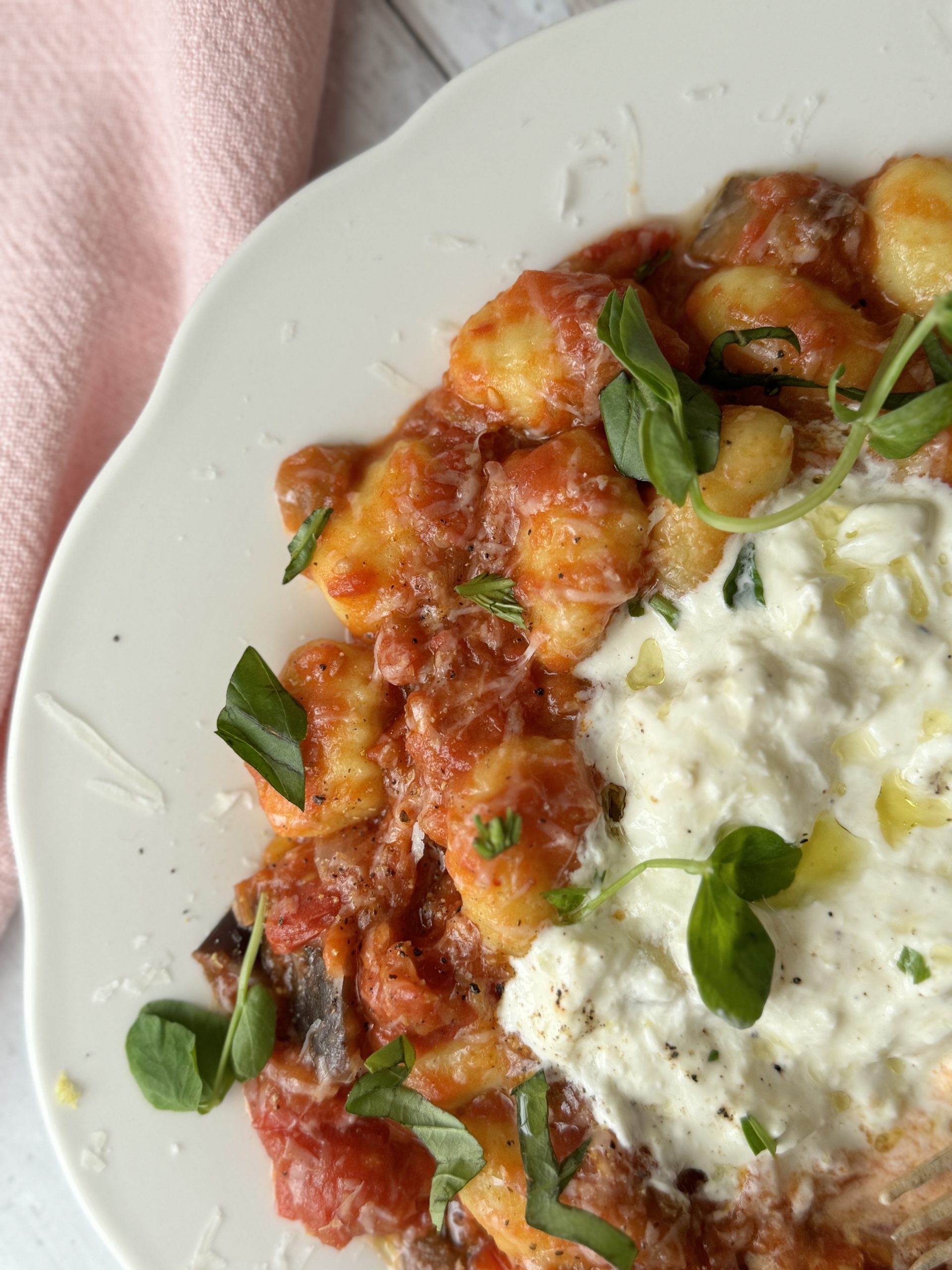 gnocchi alla norma on a white plate with burrata and fresh basil on top