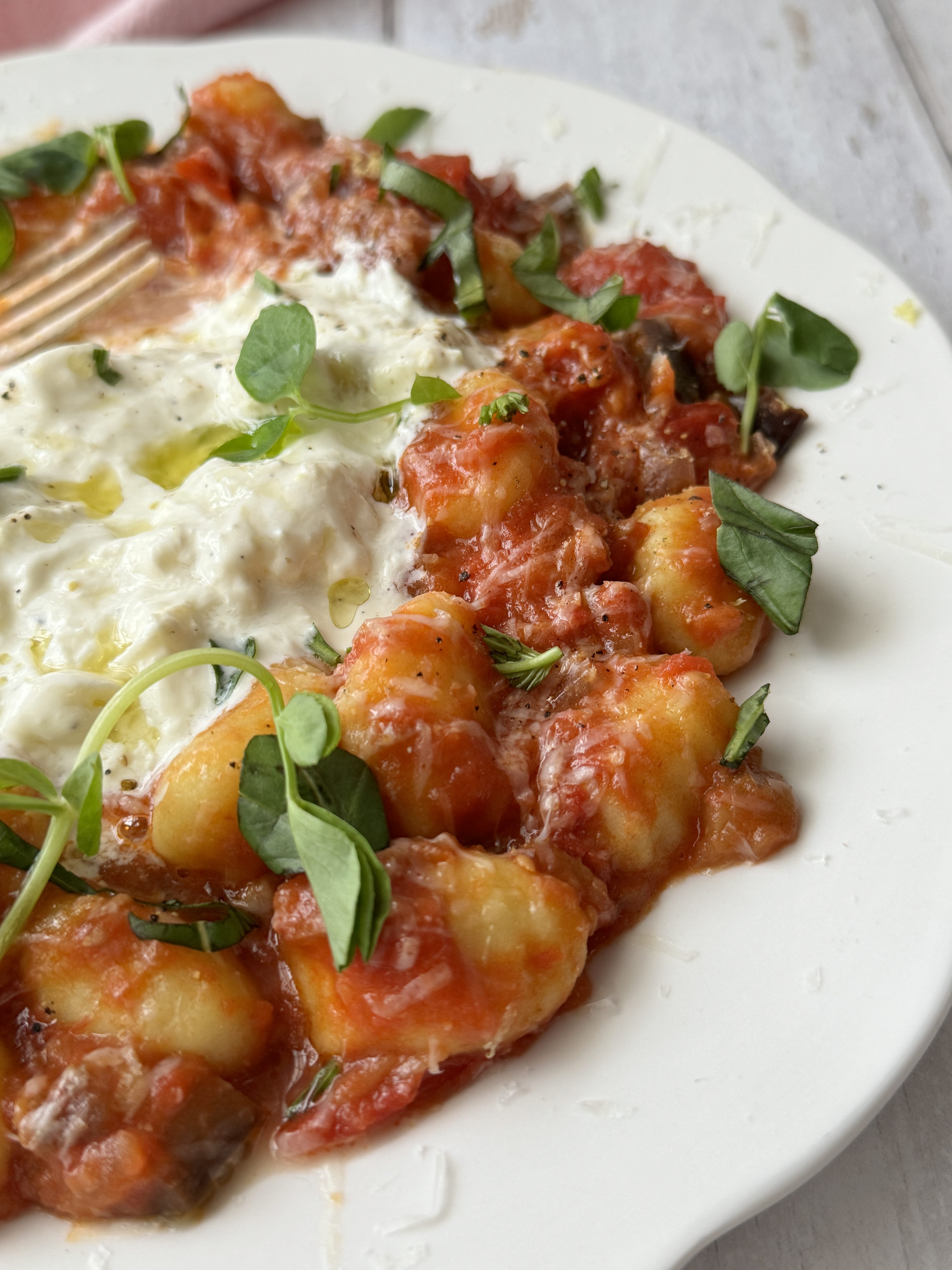 gnocchi alla norma on a white plate with burrata and fresh basil on top