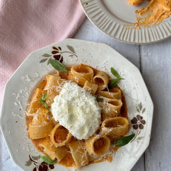 a white bowl filled with tomato butter pasta and topped with burrata