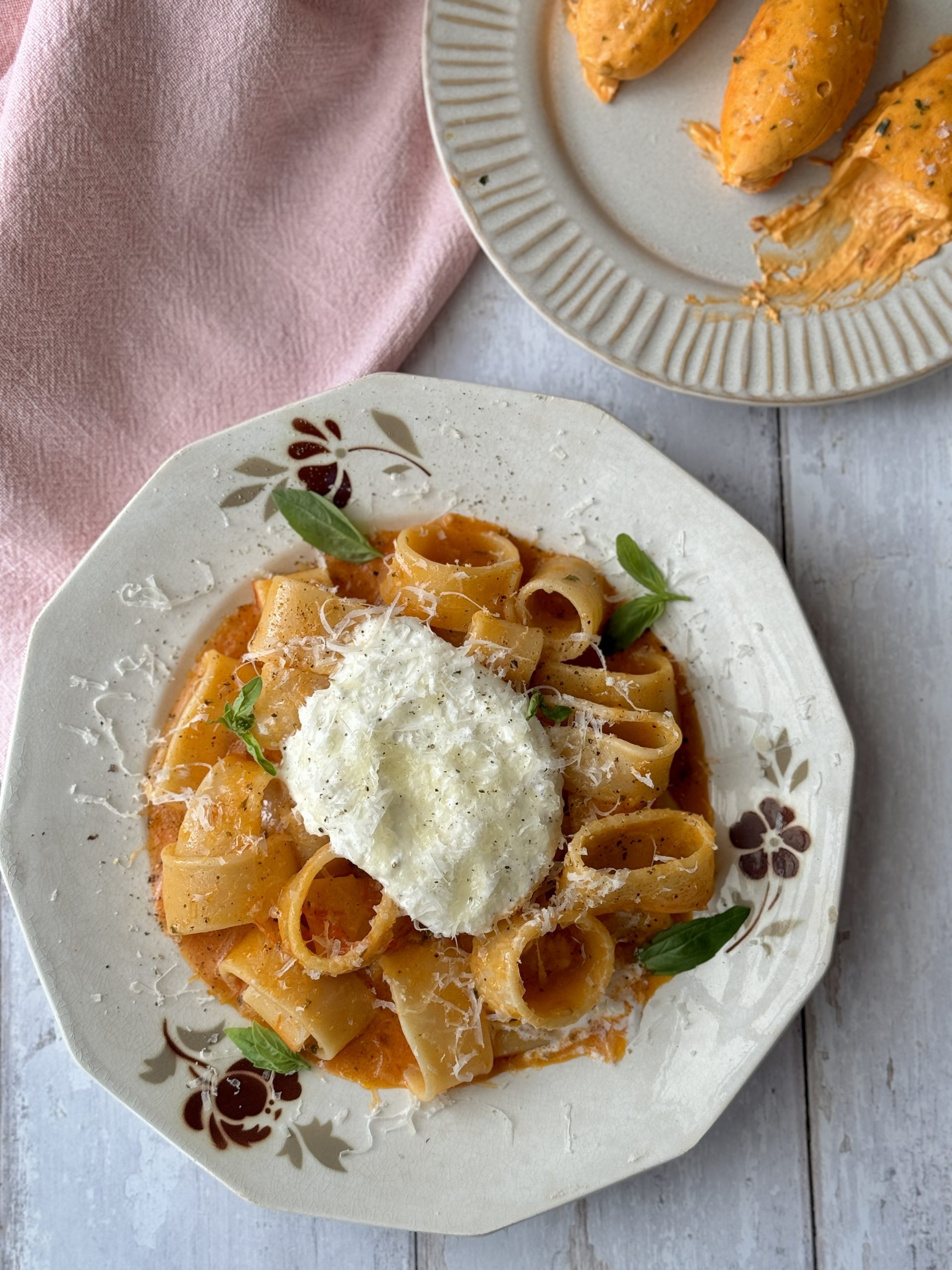 a white bowl filled with tomato butter pasta and topped with burrata