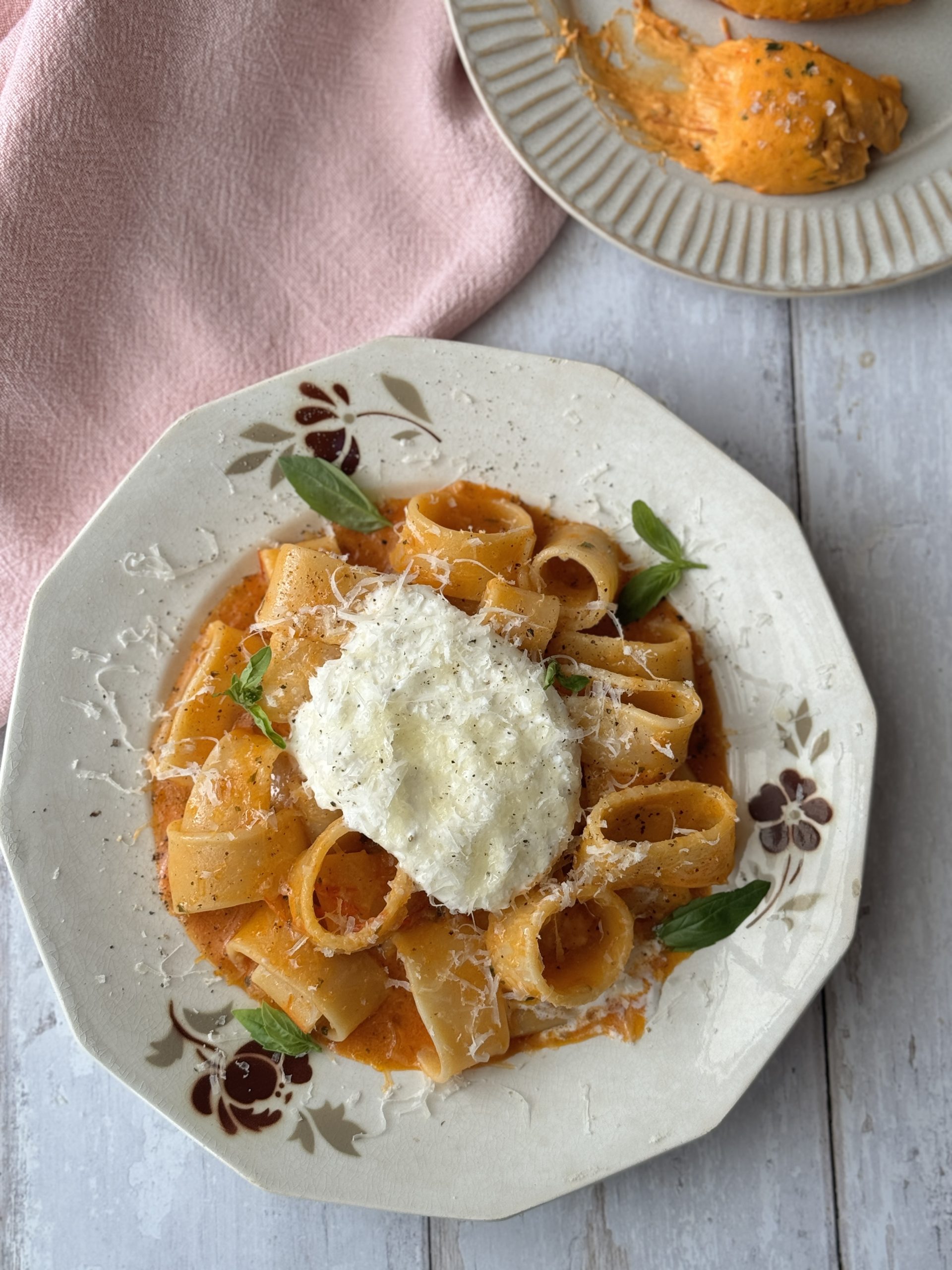 a white bowl filled with tomato butter pasta and topped with burrata