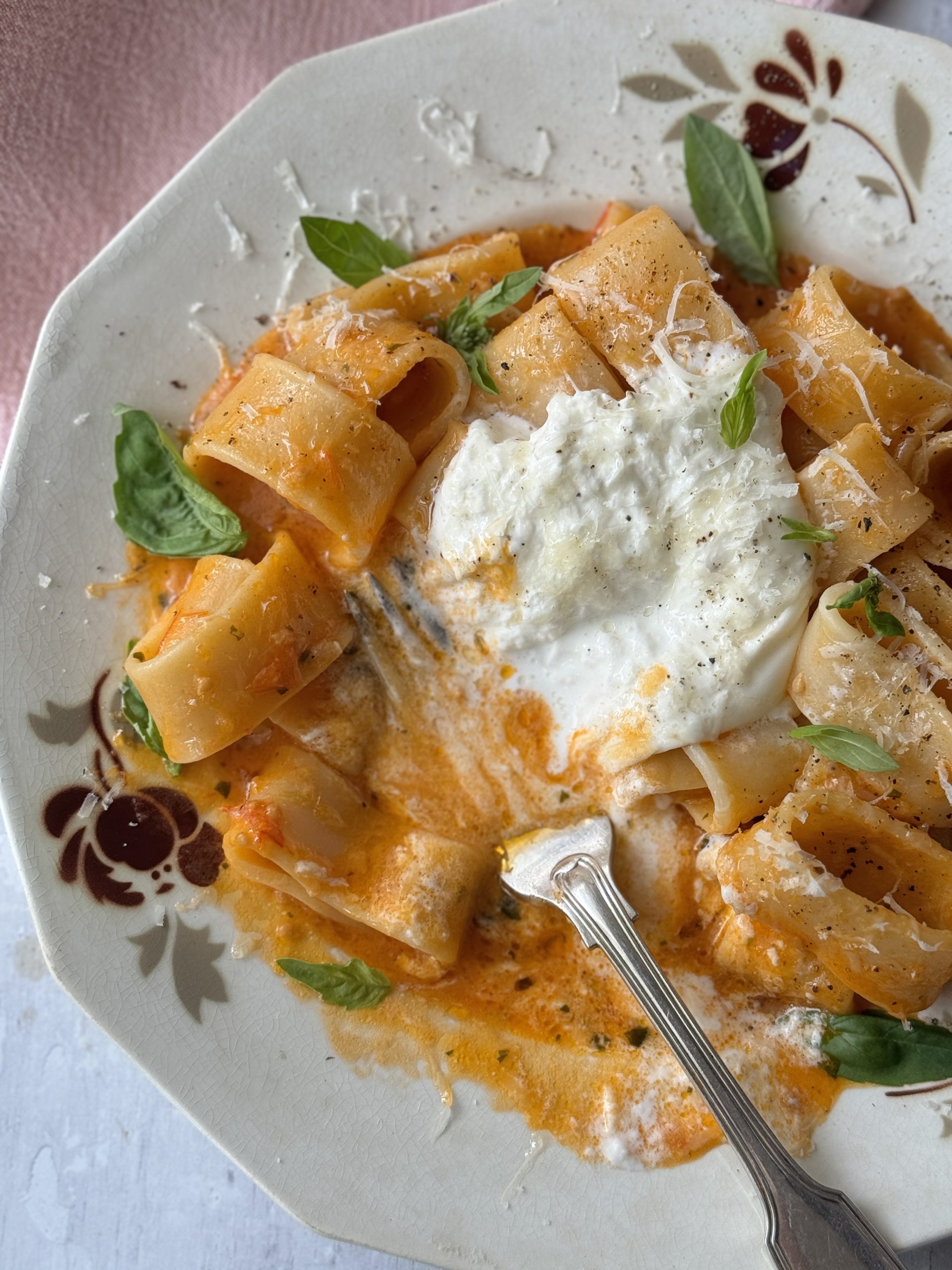 a white bowl with a fork filled with tomato butter pasta and topped with burrata