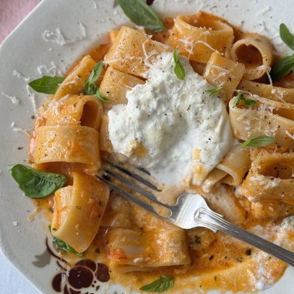 a white bowl with a fork filled with tomato butter pasta and topped with burrata