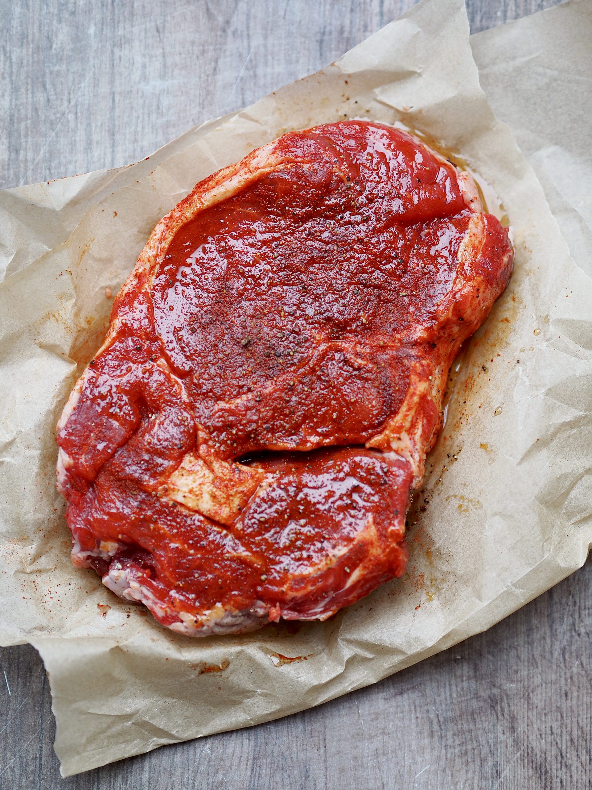 Rib eye steak on baking parchment rubbed with paprika, oil and salt.