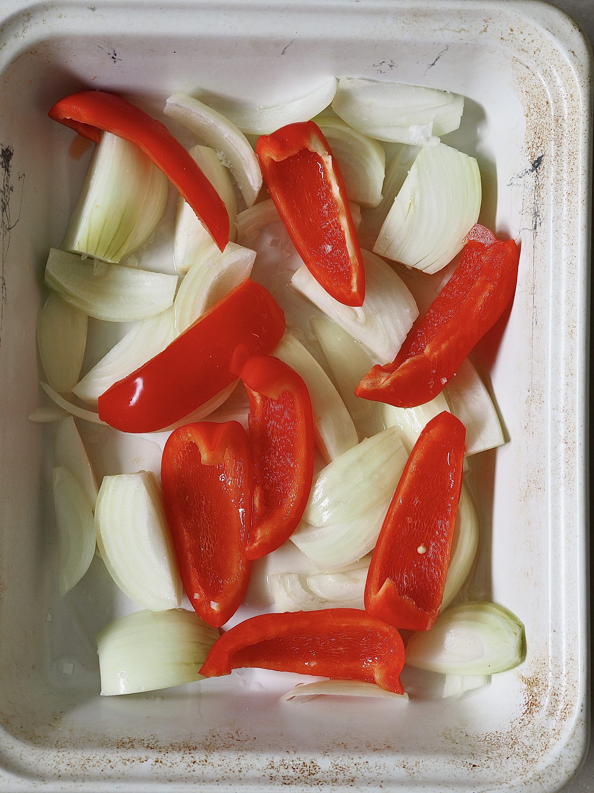 Chopped white onions and red peppers in a white roasting tray.