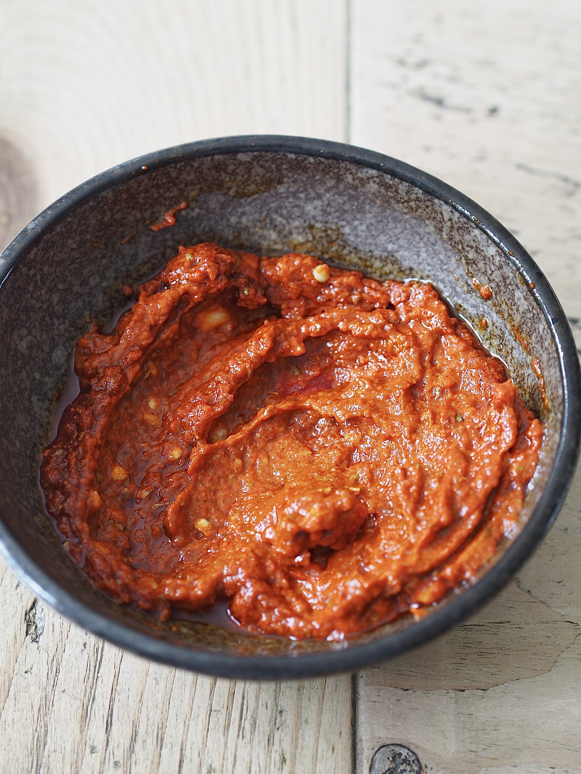 Homemade peri peri sauce in a black bowl on a wooden table.