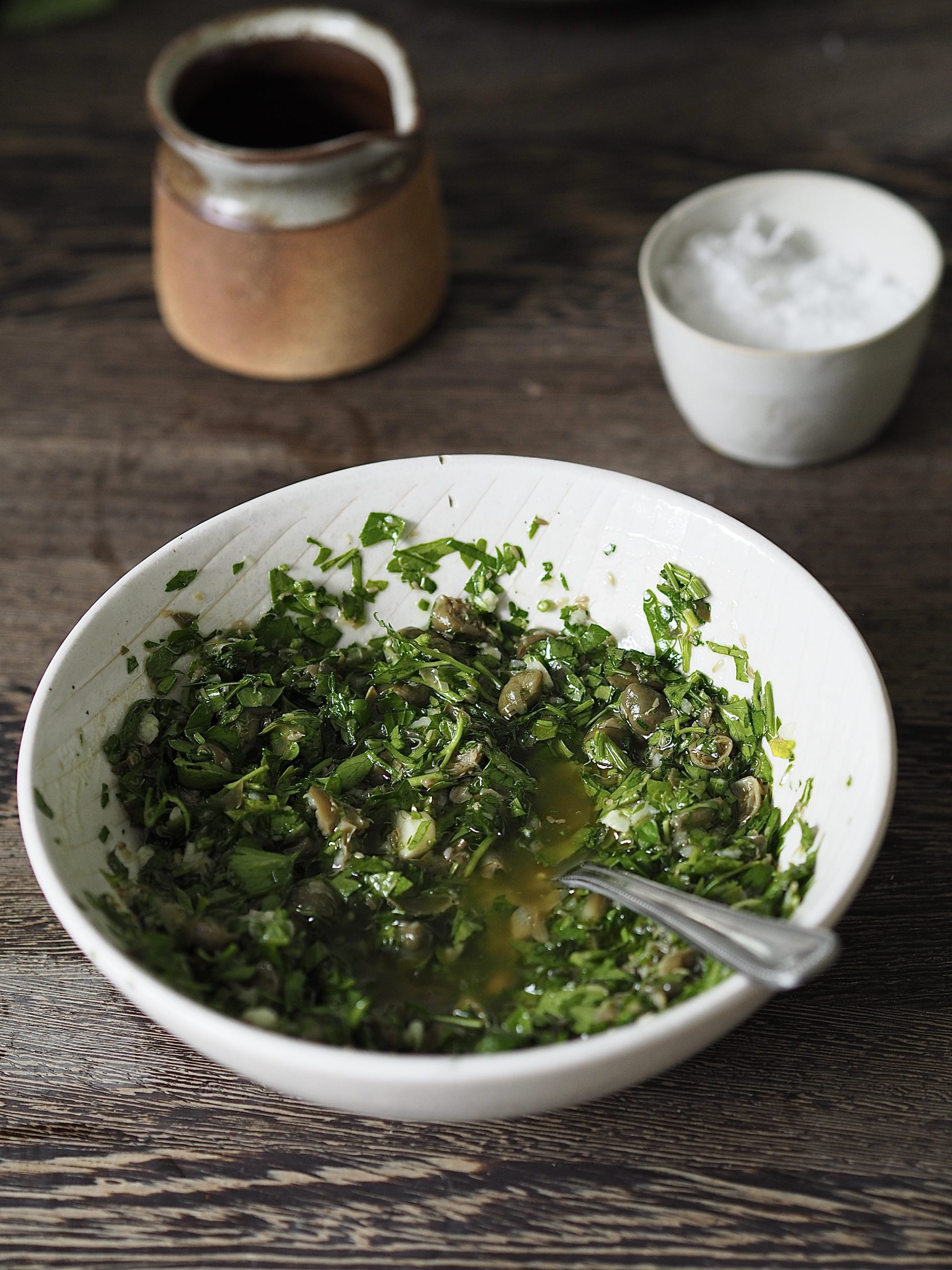 White bowl of salsa verde with a teaspoon on a wooden countertop. 