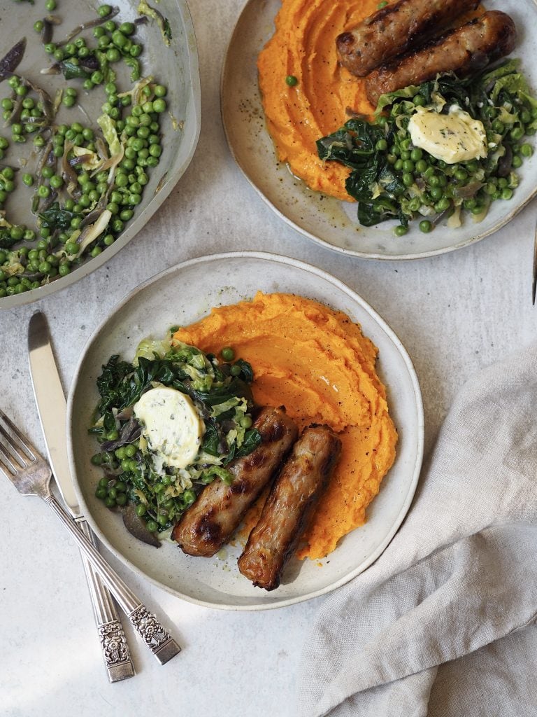 Grey plates of sweet potato mash, sausages and greens topped with a disc of garlic butter. 