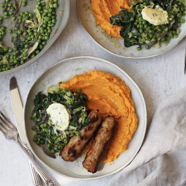 Grey plates of sweet potato mash, sausages and greens topped with a disc of garlic butter.