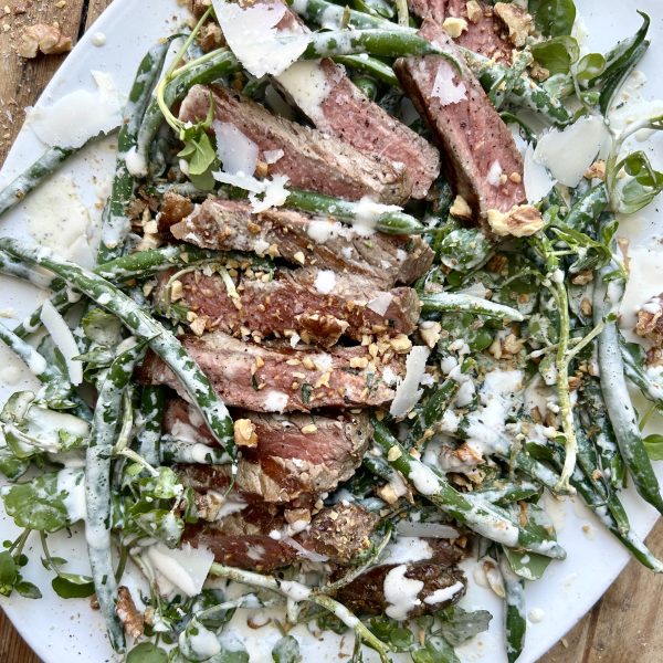 White serving platter with a steak and green bean caesar salad.