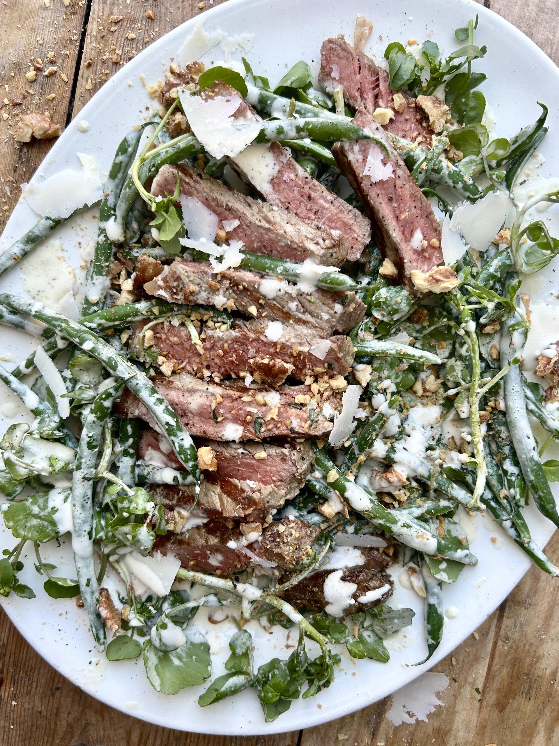 A steak and green bean salad with a creamy dressing on a white plate.