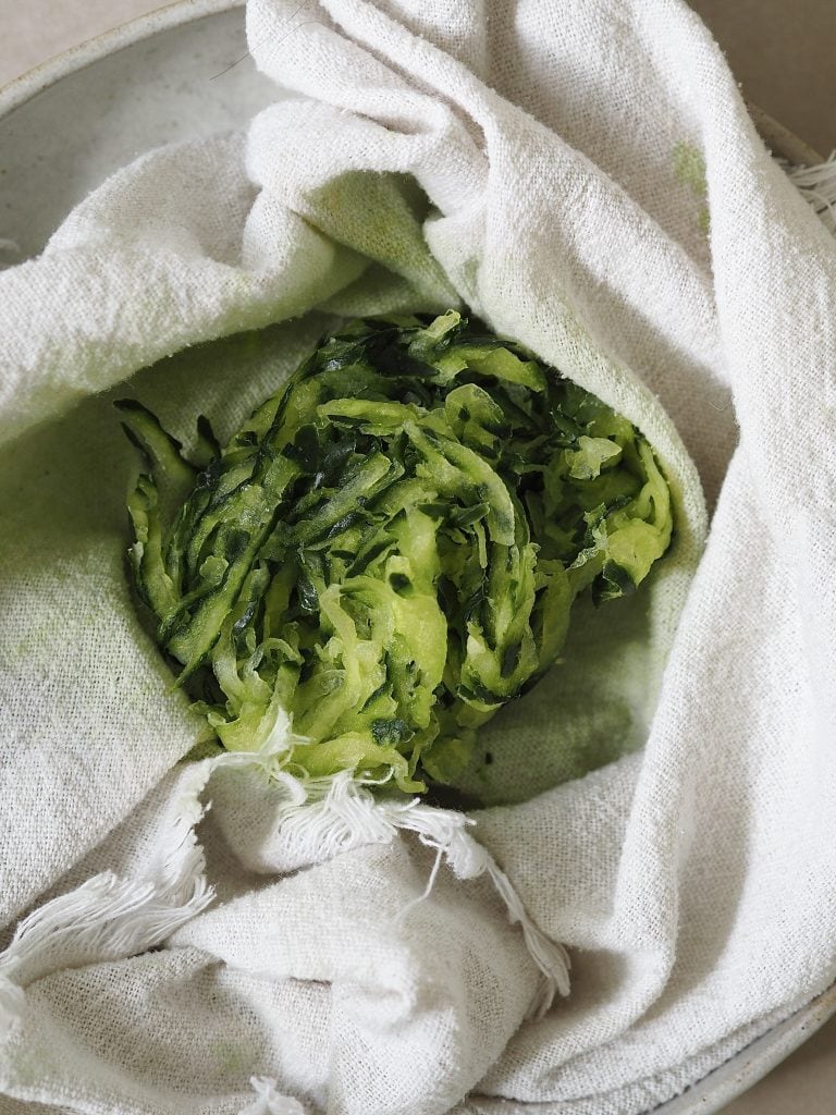 Grated cucumber being strained in a kitchen towel.