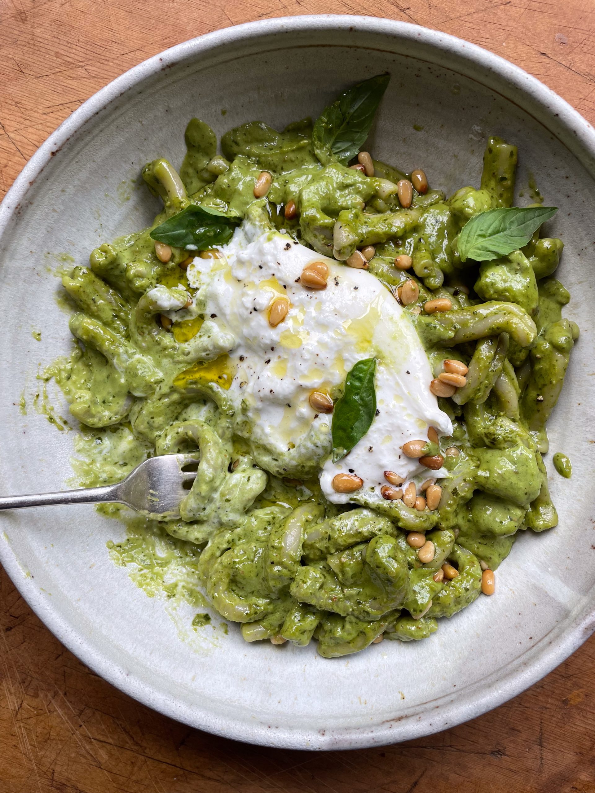 Fork twirling creamy pesto pasta in a stone bowl.