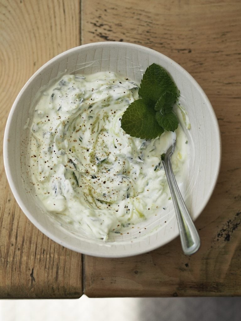 White bowl of tzatziki garnished with fresh mint.