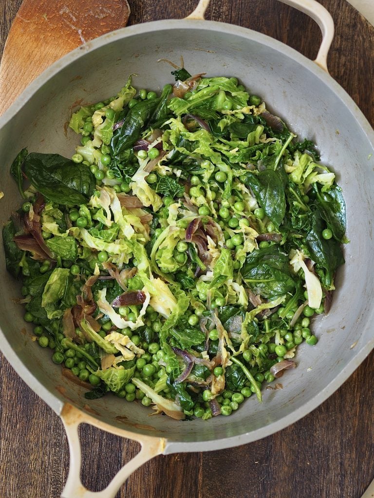 Wilted greens and peas in a frying pan.