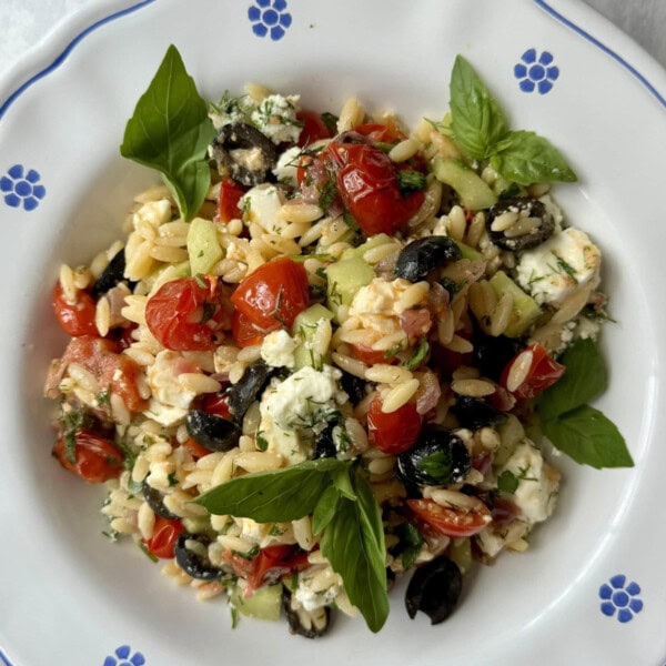 greek pasta salad in white bowl with blue flowers.