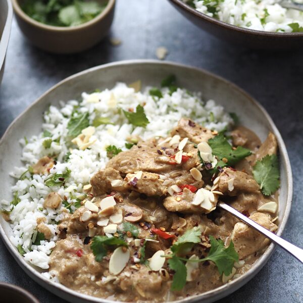 Grey bowl of white rice with coriander and chicken curry topped with toasted almonds.