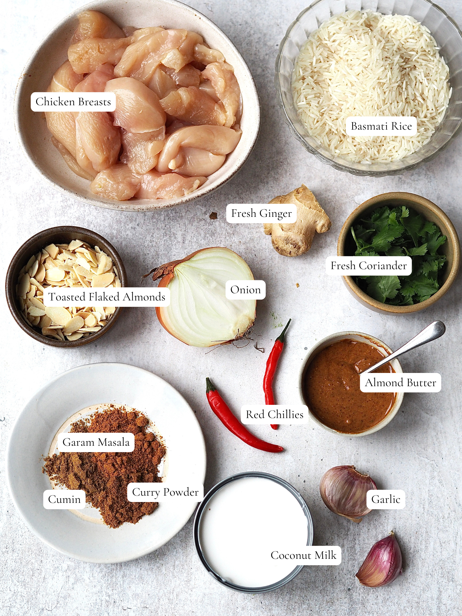 Ingredients to make an Almond Butter Chicken Curry on a grey background.